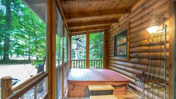 A log cabin with a wooden deck, a bench, and a window overlooking a forest. - Cozy Cabin Getaway with Private Hot Tub & Lake Access in Saugatuck! (Saugatuck)