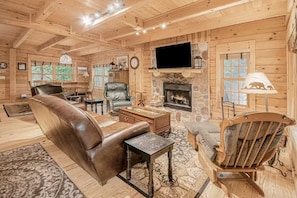 A log cabin interior with a leather sofa, a stone fireplace, and a television mounted above it.