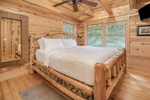 A wooden cabin bedroom with a bed, a ceiling fan, and windows. - Hidden Dunes #11 (Saugatuck)