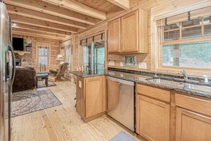 A wooden cabin interior with a kitchen, dining area, and a fireplace.