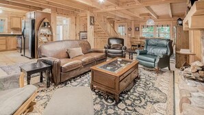 A spacious wooden cabin interior with a leather sofa, a glass-top coffee table, and a stone fireplace. - Cozy Cabin Getaway with Private Hot Tub & Lake Access in Saugatuck! (Saugatuck)