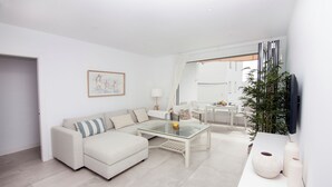 A modern living room with a sectional sofa, a glass coffee table, and a flat-screen TV mounted on the wall. - Overlooking the sea! New apt. with terrace 3 bedrooms+2 bathrooms&community pool (Los Caños de Meca)