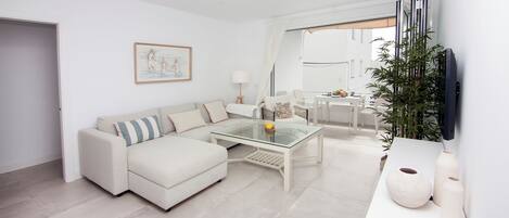 A modern living room with a sectional sofa, a glass coffee table, and a flat-screen TV mounted on the wall.