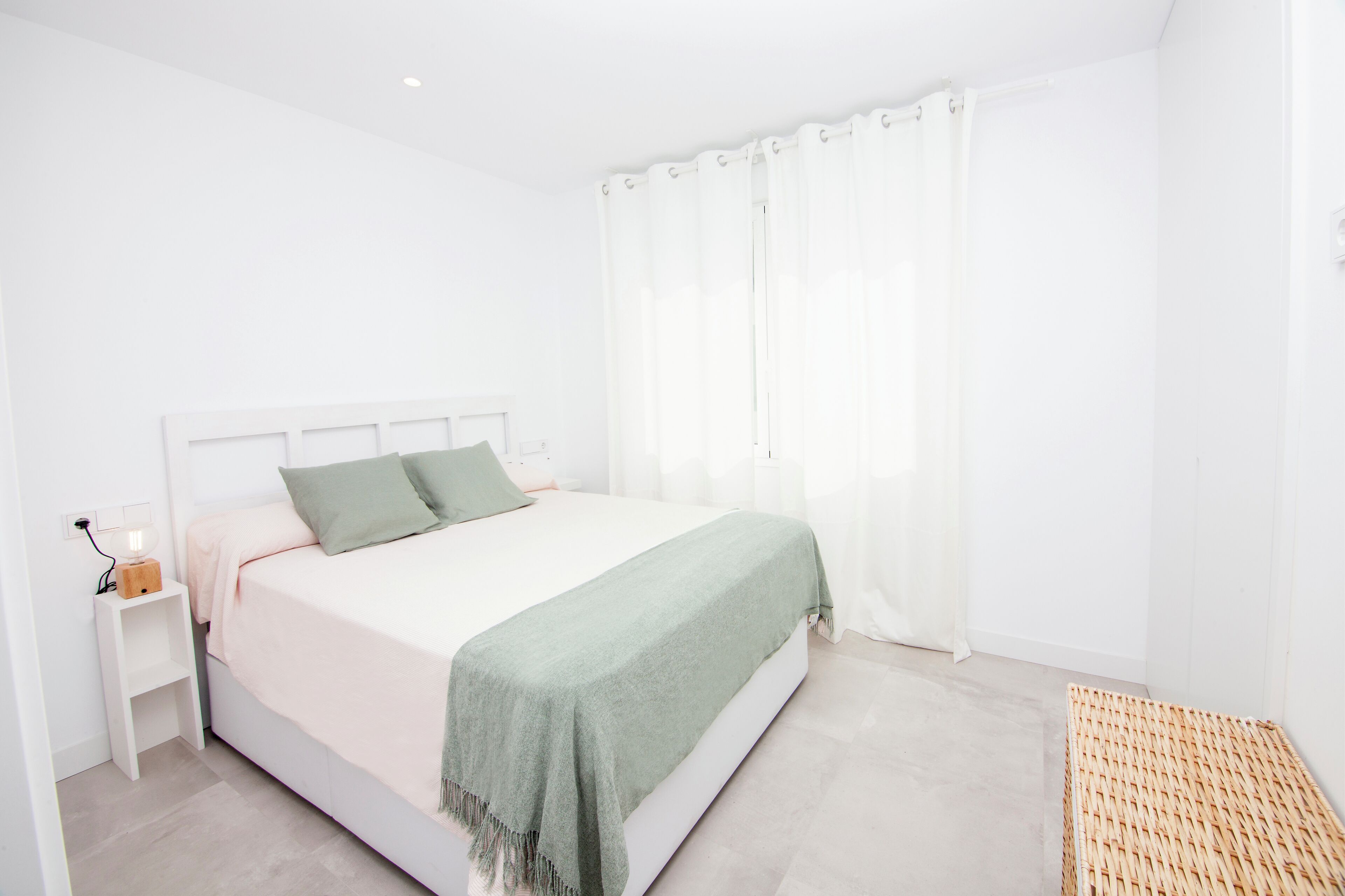 A minimalist bedroom with a bed, bedside table, and a woven mat.