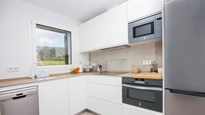 A modern kitchen with white cabinets, stainless steel appliances, and a window overlooking a green landscape. - Overlooking the sea! New apt. with terrace 3 bedrooms+2 bathrooms&community pool (Los Caños de Meca)