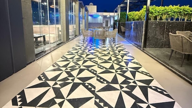 A modern outdoor patio with geometric patterned flooring, glass walls, and outdoor seating. - Shrigo Hotels Banaras (Varanasi)