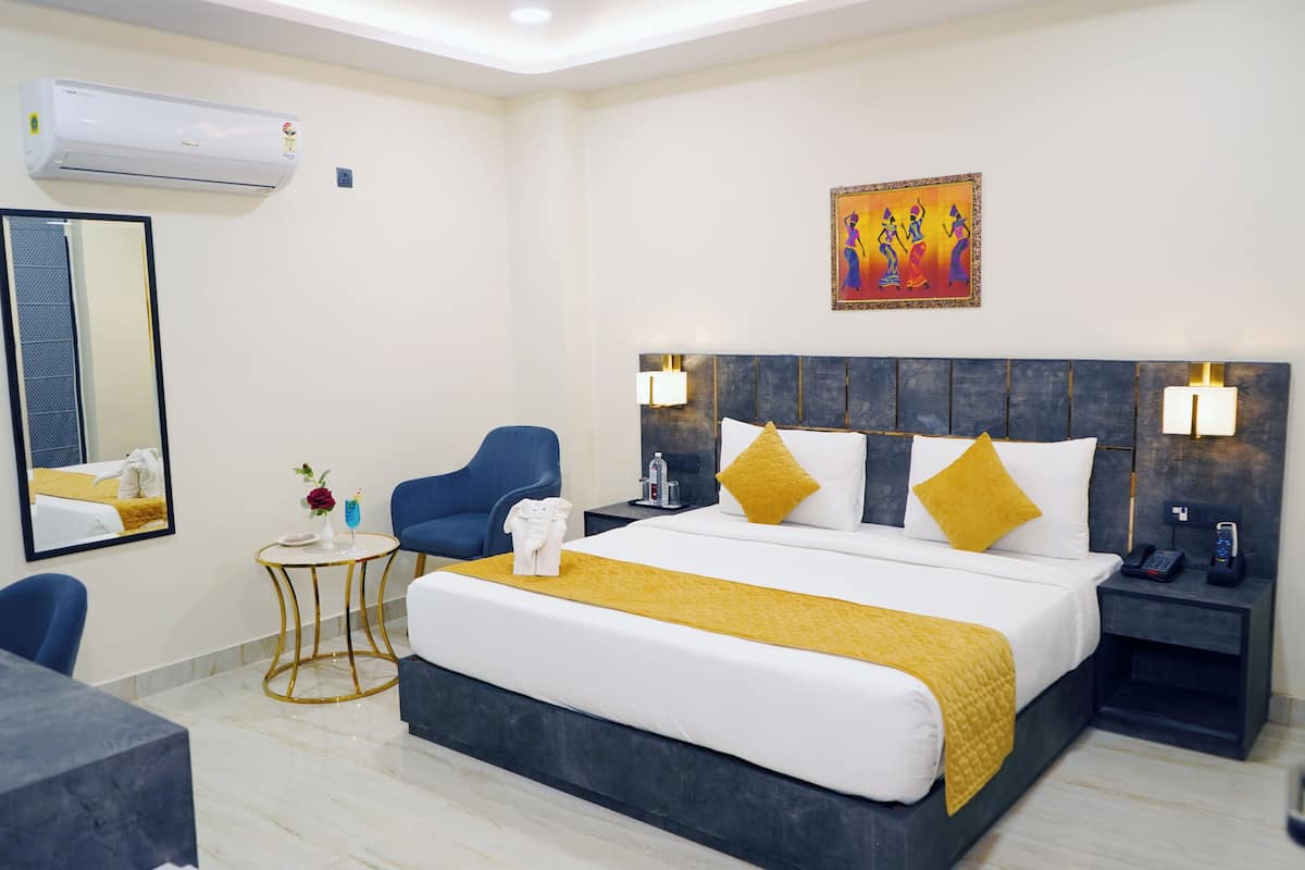 Une chambre d’hôtel avec un grand lit, un bureau, une chaise, une petite table ronde et une table de chevet avec un téléphone.