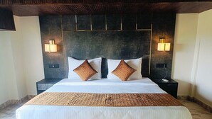 A large bed with two pillows, a bedside table, and two wall-mounted lamps. - Shrigo Hotels Banaras (Varanasi)