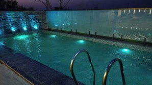 A swimming pool with a waterfall feature and illuminated steps. - Shrigo Hotels Banaras (Varanasi)