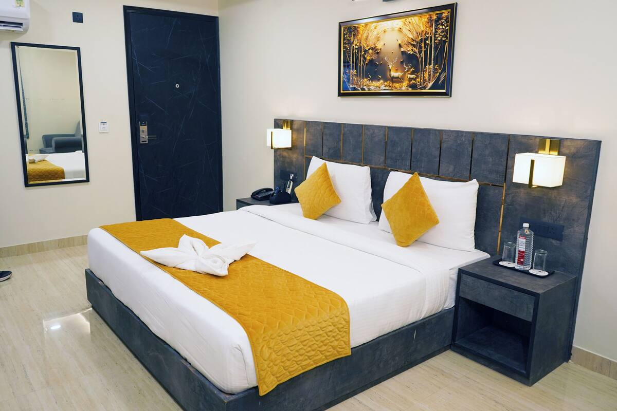 Une chambre d’hôtel avec un grand lit, une tête de lit sombre, deux lampes de chevet, une table de chevet, un miroir et une œuvre d’art encadrée accrochée au mur.