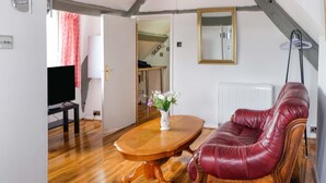 A living room with a wooden coffee table, a red leather sofa, a television, and a vase with flowers. - Host Stay Apartment 6 Church Walk (Melksham)