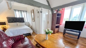 A bedroom with a bed, a wooden coffee table, a red leather sofa, a TV, and a window with curtains. - Host Stay Apartment 6 Church Walk (Melksham)