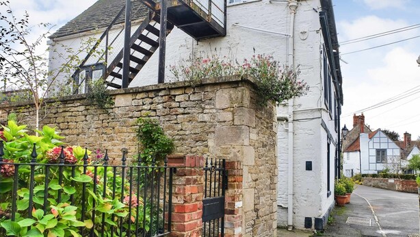 A white building with a stone wall, a black metal staircase, and a brick gate. - Host Stay Apartment 6 Church Walk (Melksham)