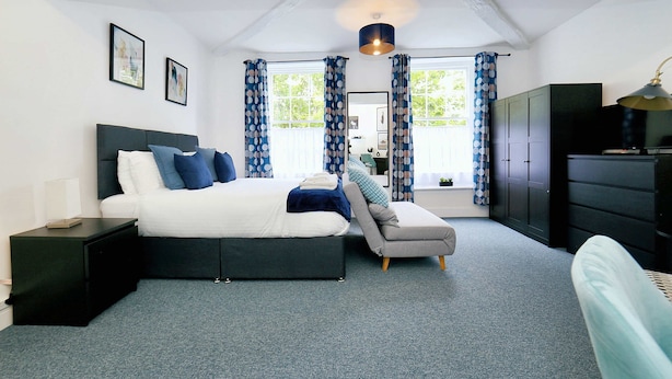 Une chambre à coucher comprenant un lit, une table de chevet, une commode et donnant sur l’extérieur.