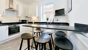Une cuisine moderne avec des meubles blancs, un plan de travail noir et quatre tabourets noirs.