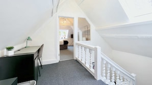 Un escalier avec une rampe blanche mène à une pièce où se trouvent un bureau et une chaise.