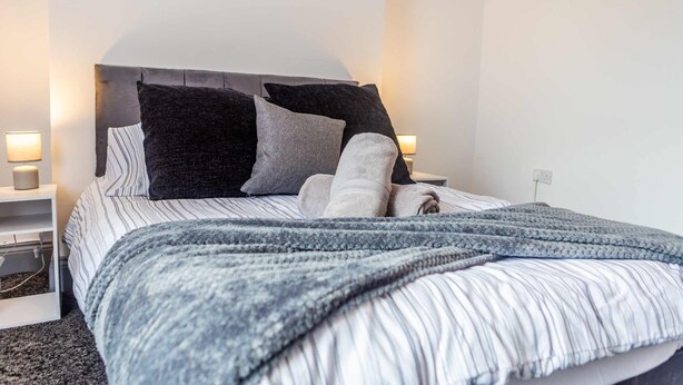 A neatly made bed with striped bedding, a grey knitted blanket, and two bedside lamps. - Host Stay Bambro Apartment (Sunderland)
