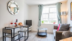 A modern living room with a dining area, a round table, a sofa, and a TV. - Host Stay Croydon Road Apartment (Caterham)