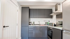 A compact kitchen with grey cabinets, a stainless steel oven, and a white door. - Host Stay Croydon Road Apartment (Caterham)