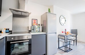 Eine kompakte Küche mit Einbauofen, Kühlschrank und Mikrowelle. Ein kleiner Essbereich mit Tisch und Stühlen ist ebenfalls vorhanden.