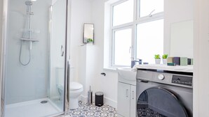 A modern bathroom with a glass-enclosed shower, a toilet, a sink, and a washing machine. - Host Stay Croydon Road Apartment (Caterham)