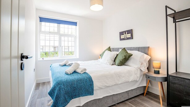 A bedroom with a bed, a window with a view, a bedside table with a lamp, and a door. - Host Stay Croydon Road Apartment (Caterham)