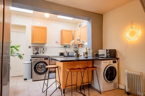 A compact kitchen with a washing machine, a microwave, wooden stools, and a small bar area.