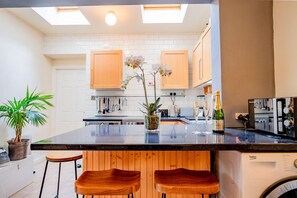 A modern kitchen with white cabinets, a black countertop, and wooden stools. - Host Stay Over the Bridge Cottage (Leominster)