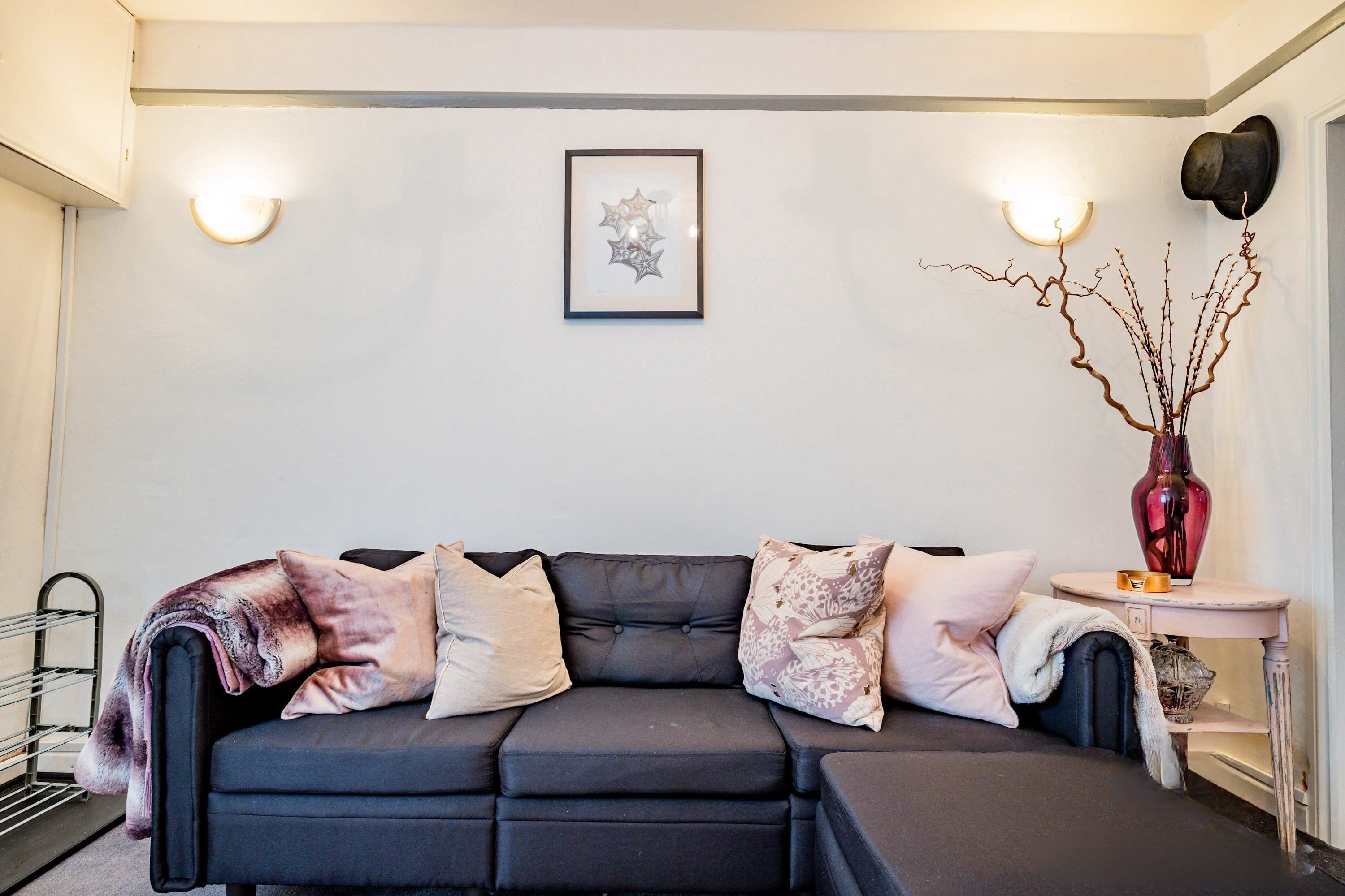 Ein modernes Wohnzimmer mit einem dunkelgrauen Ecksofa, einem kleinen Beistelltisch mit einer Vase und einem gerahmten Kunstwerk an der Wand.