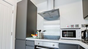 A modern kitchen with a microwave, oven, and a glass bowl with fruits on the counter. - Host Stay Croydon Road Dwelling (Caterham)