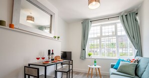 Een moderne woonkamer met een eethoek, een bank, een televisie en een raam met gordijnen.