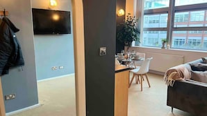 A modern living room with a TV mounted on the wall, a dining area with a table set for two, and a large window offering a view of the cityscape. - Host Stay Great Hampton Apartment (Birmingham)