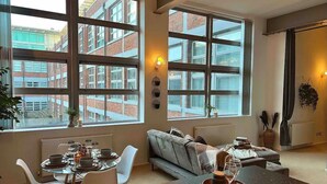 A modern living room with large windows, a dining area, and a sofa. - Host Stay Great Hampton Apartment (Birmingham)