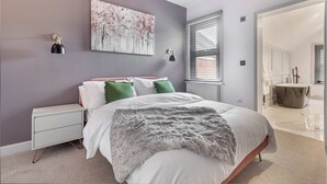 A bedroom with a bed, bedside table, artwork, and a view of the bathroom. - Host Stay Barton Road Retreat (Hereford)