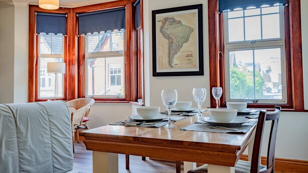 A dining area with a wooden table set for four, two chairs, and a map on the wall. - Host Stay Wellington Apartment (Horsham)