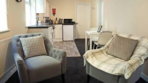 A compact living space with a kitchenette, two armchairs, a dining table, and a door leading to another room. - Host Stay Clacton Waves (Clacton-on-Sea)