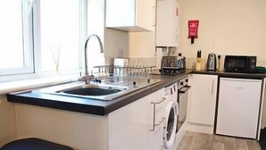 A compact kitchen with a sink, stove, microwave, and a washing machine. - Host Stay Clacton Waves (Clacton-on-Sea)