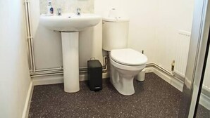 A small bathroom with a white sink, toilet, and a black trash bin. - Host Stay Clacton Waves (Clacton-on-Sea)
