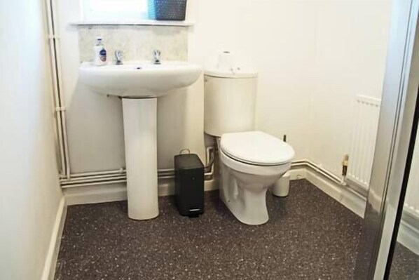 A small bathroom with a white sink, toilet, and a black trash bin. - Host Stay Clacton Waves (Clacton-on-Sea)