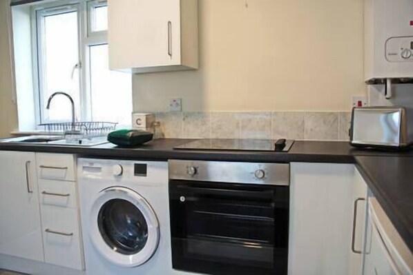 A compact kitchen with a washing machine, oven, and a toaster. - Host Stay Clacton Waves (Clacton-on-Sea)