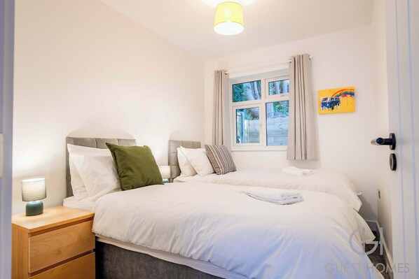 A neatly arranged bedroom with a bed, bedside table, and a window with curtains. - Host Stay Croydon Road Abode (Caterham)