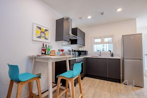 A modern kitchen with dark cabinets, a stainless steel refrigerator, and a bar area with two stools. - Host Stay Croydon Road Abode (Caterham)