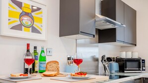 A modern kitchen with a dining table set for two, featuring bread, tomatoes, and wine glasses. - Host Stay Croydon Road Abode (Caterham)