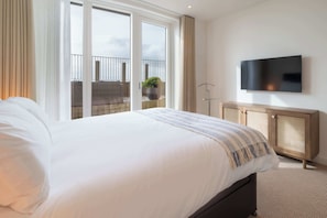 A hotel room with a large bed, a TV mounted on the wall, and a balcony with a potted plant.