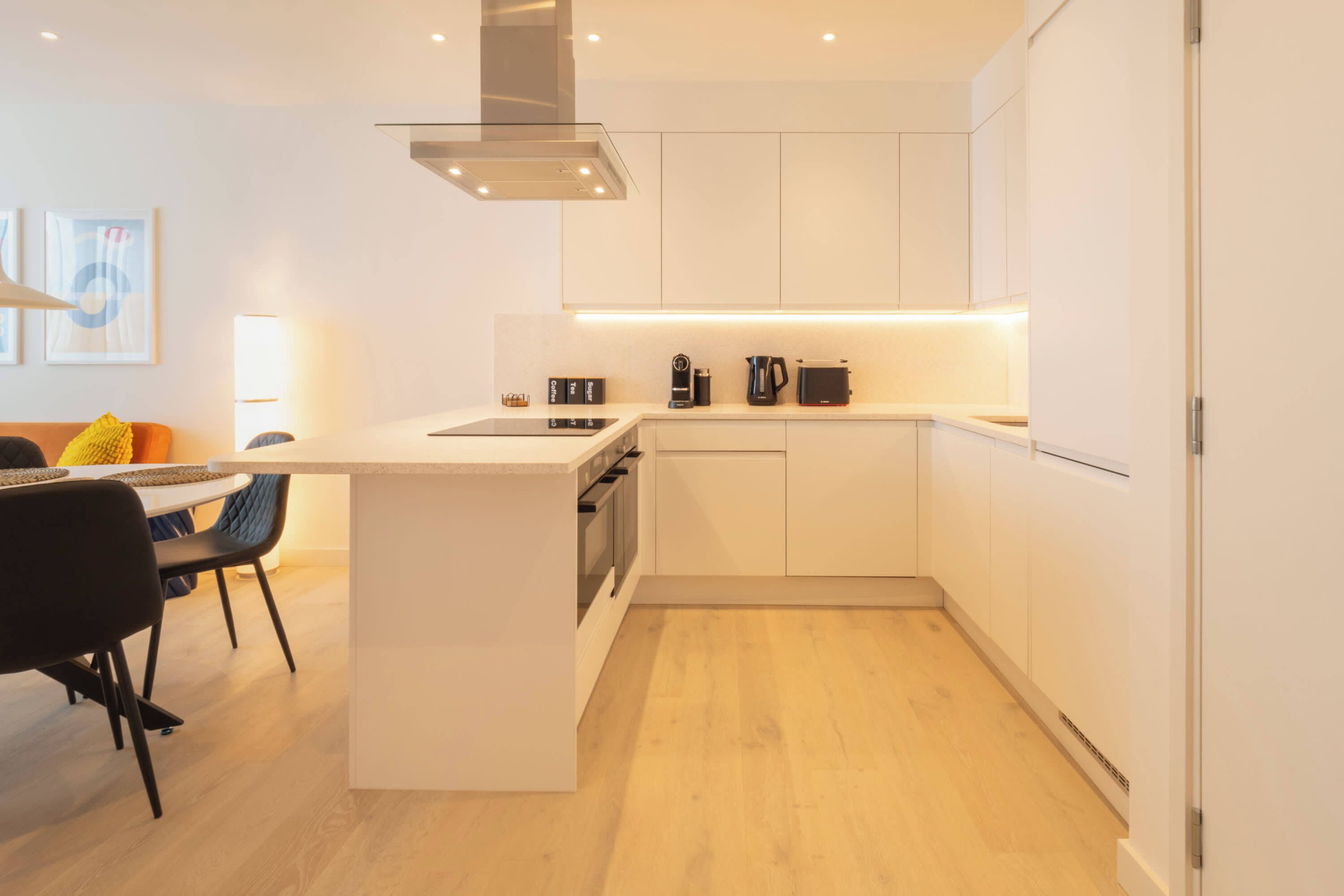 Een moderne keuken met witte kasten, een centraal eiland en een eethoek met een tafel en stoelen.