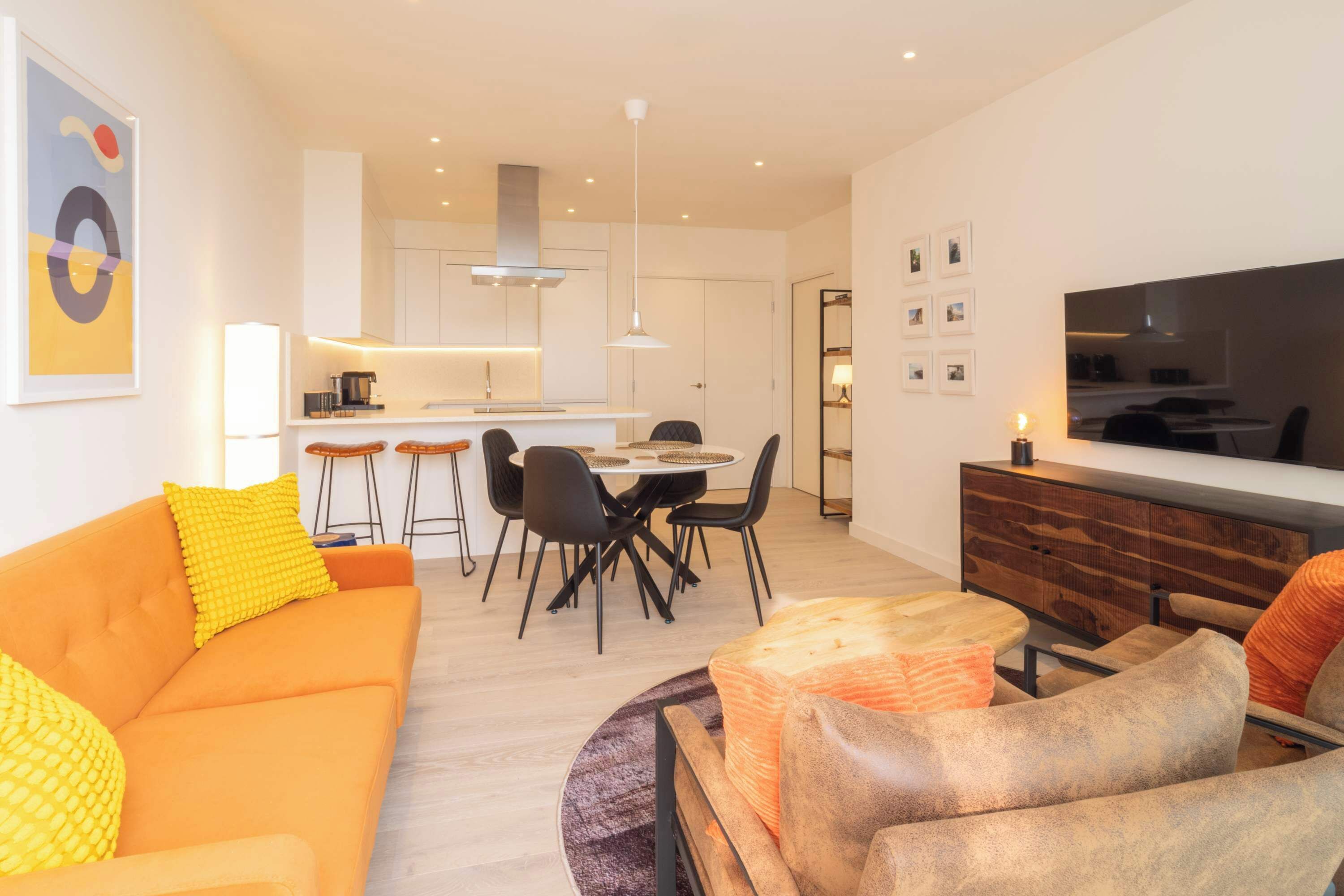 Una sala de estar moderna con un sofá, una mesa de centro y un televisor. Hay un comedor con sillas y una mesa.