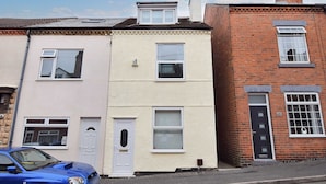 A row of terraced houses with distinct front doors and windows, a clear sky, and a parked car. - Host Stay Church Drive (Mansfield)
