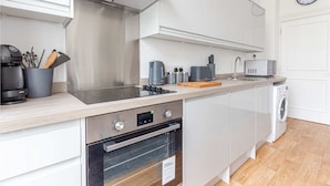 Una cocina moderna con gabinetes blancos, una campana extractora de acero inoxidable, horno empotrado, microondas y lavavajillas.