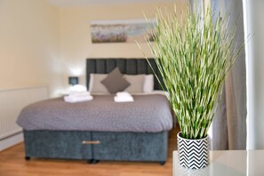 A bedroom with a bed, a bedside table, and a potted plant.