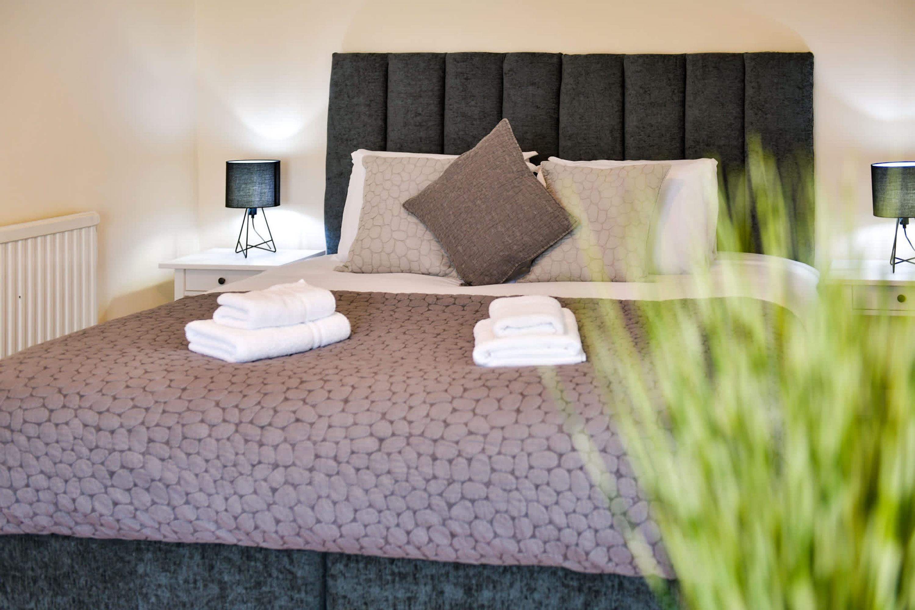 A neatly made bed with a patterned bedspread, two bedside tables with lamps, and a radiator.